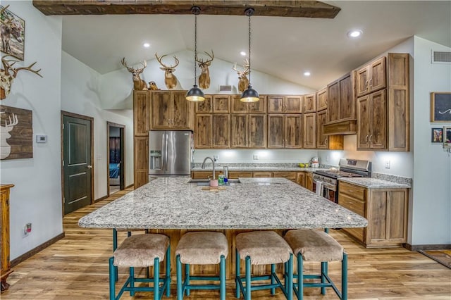 kitchen with a breakfast bar, a sink, hanging light fixtures, appliances with stainless steel finishes, and an island with sink