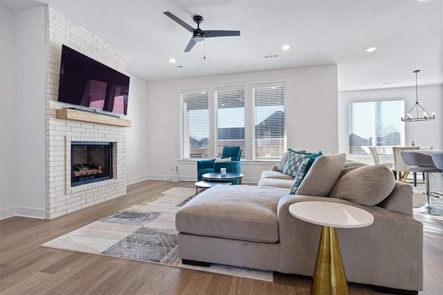 living room with ceiling fan with notable chandelier, light hardwood / wood-style floors, and a brick fireplace