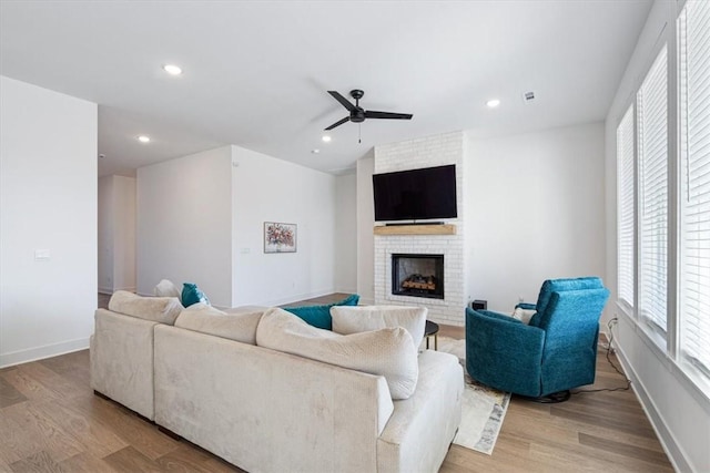 living room featuring ceiling fan, light hardwood / wood-style floors, and a brick fireplace