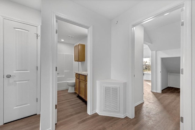 hall with wood finished floors, visible vents, and baseboards