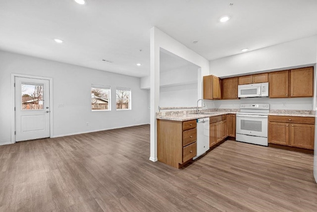 kitchen with a sink, wood finished floors, recessed lighting, white appliances, and brown cabinetry