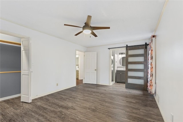 unfurnished bedroom featuring ensuite bath, ceiling fan, a barn door, dark hardwood / wood-style flooring, and crown molding