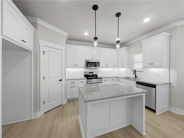 kitchen with light stone countertops, appliances with stainless steel finishes, a kitchen island, sink, and white cabinetry