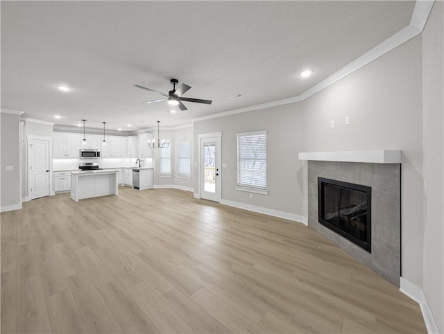 unfurnished living room with a tile fireplace, ceiling fan with notable chandelier, sink, light hardwood / wood-style flooring, and ornamental molding