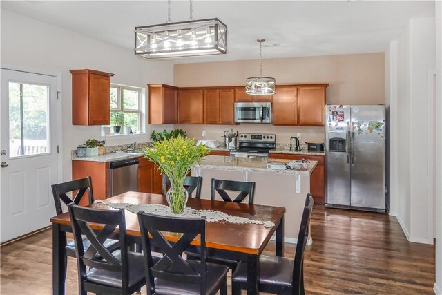 kitchen featuring appliances with stainless steel finishes, light stone counters, dark wood-type flooring, pendant lighting, and a kitchen island