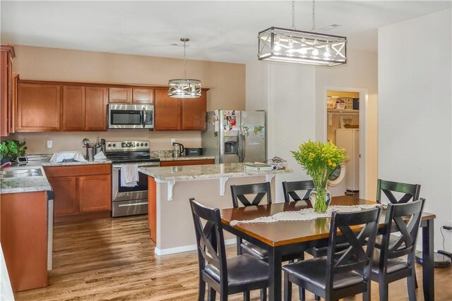 kitchen with light stone countertops, hanging light fixtures, a breakfast bar, appliances with stainless steel finishes, and light wood-type flooring