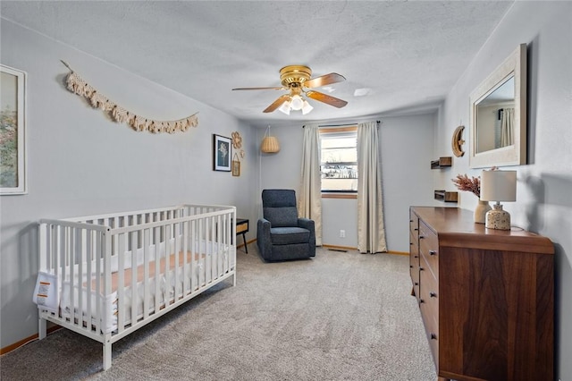 carpeted bedroom with a crib, a textured ceiling, and ceiling fan