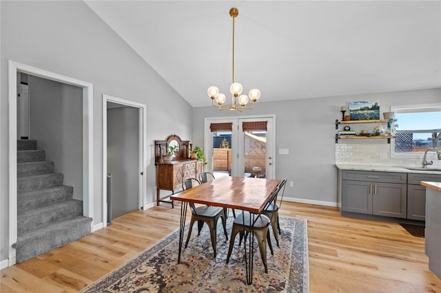 dining area with sink, light hardwood / wood-style floors, vaulted ceiling, and a notable chandelier