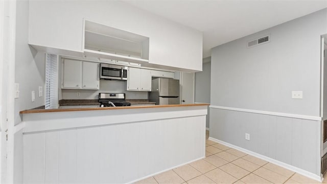 kitchen with kitchen peninsula, light tile patterned flooring, stainless steel appliances, and white cabinetry