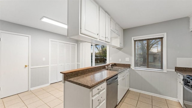 kitchen with white cabinets, stainless steel appliances, wooden walls, sink, and light tile patterned floors