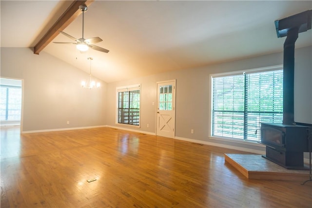 unfurnished living room with ceiling fan with notable chandelier, a wood stove, wood-type flooring, and lofted ceiling with beams