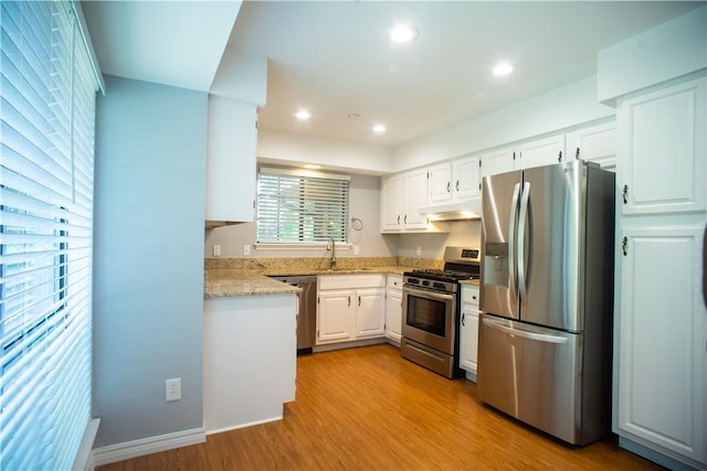 kitchen with appliances with stainless steel finishes, white cabinets, light stone countertops, light hardwood / wood-style flooring, and sink