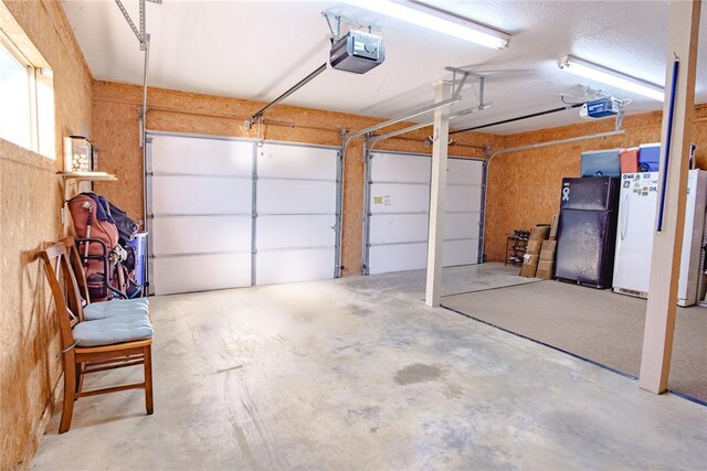 garage featuring white fridge, black refrigerator, and a garage door opener