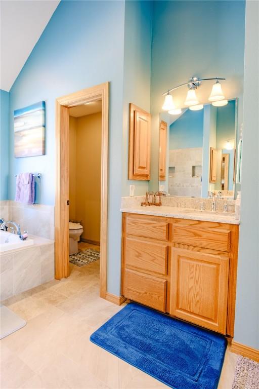 bathroom featuring a relaxing tiled tub, vaulted ceiling, toilet, tile patterned floors, and vanity