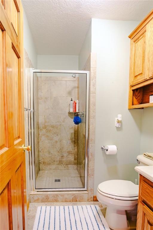 bathroom with a textured ceiling, vanity, a shower with shower door, and toilet