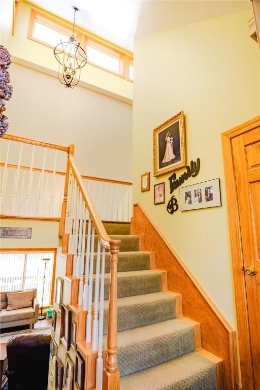 stairs featuring a high ceiling, wood walls, plenty of natural light, and a notable chandelier