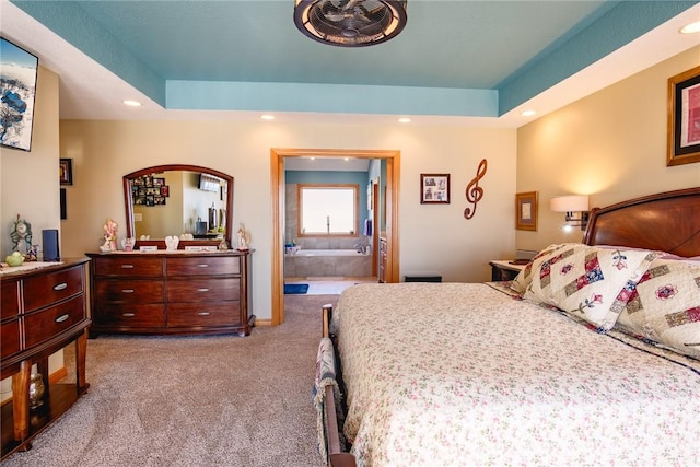 bedroom with ensuite bathroom, a raised ceiling, and light carpet