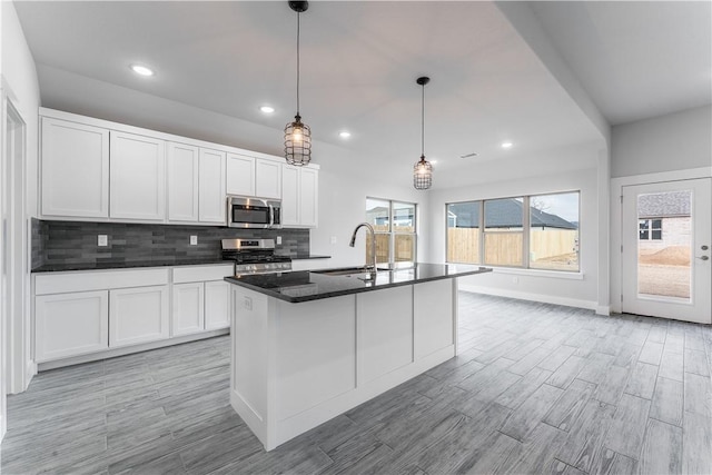 kitchen featuring stainless steel appliances, a center island with sink, white cabinetry, and hanging light fixtures