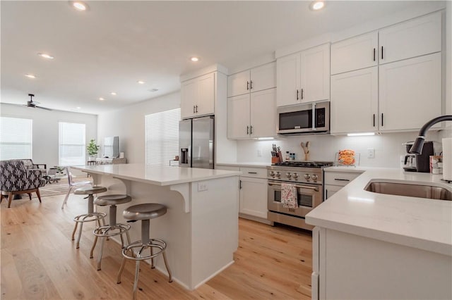 kitchen with stainless steel appliances, white cabinetry, a center island, and light wood-type flooring