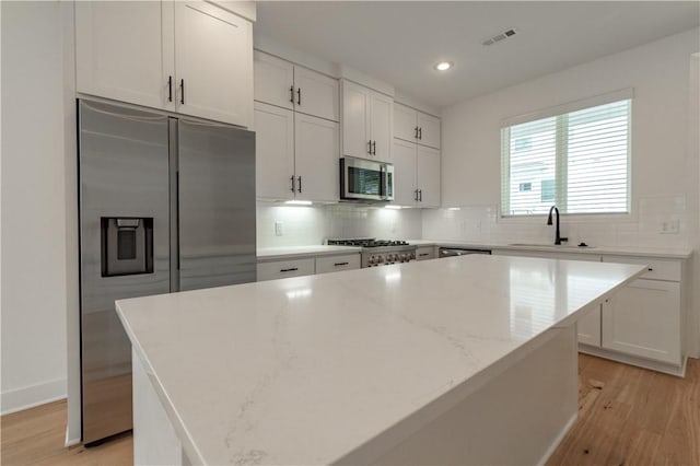 kitchen featuring appliances with stainless steel finishes, white cabinets, light wood-type flooring, and a center island