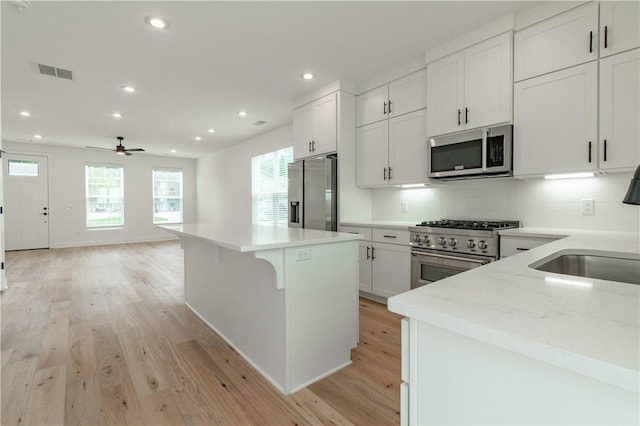 kitchen with white cabinets, ceiling fan, light wood-type flooring, light stone countertops, and appliances with stainless steel finishes