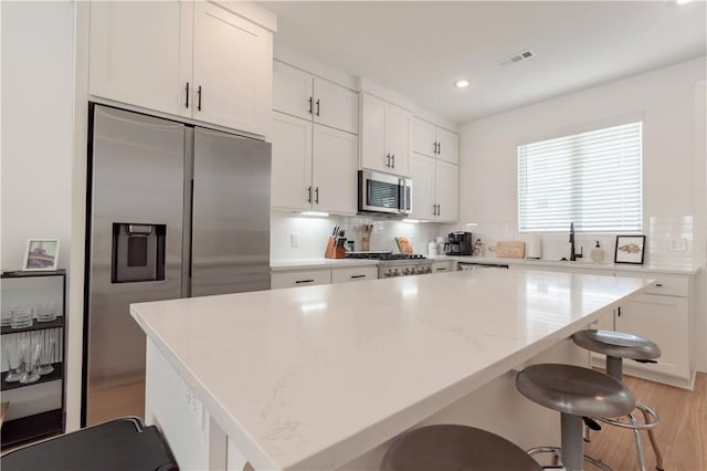 kitchen featuring stainless steel appliances, white cabinets, a center island, and light stone counters