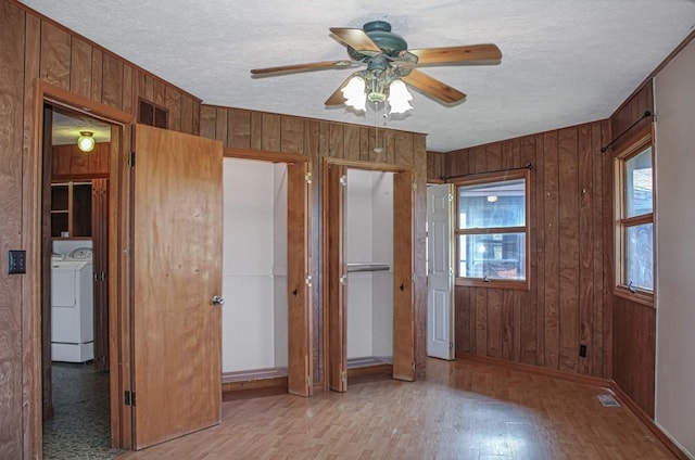 unfurnished bedroom featuring a textured ceiling, washing machine and dryer, wood walls, light hardwood / wood-style floors, and ceiling fan