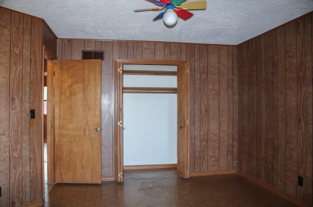 unfurnished room featuring a textured ceiling, ceiling fan, wooden walls, and dark parquet floors