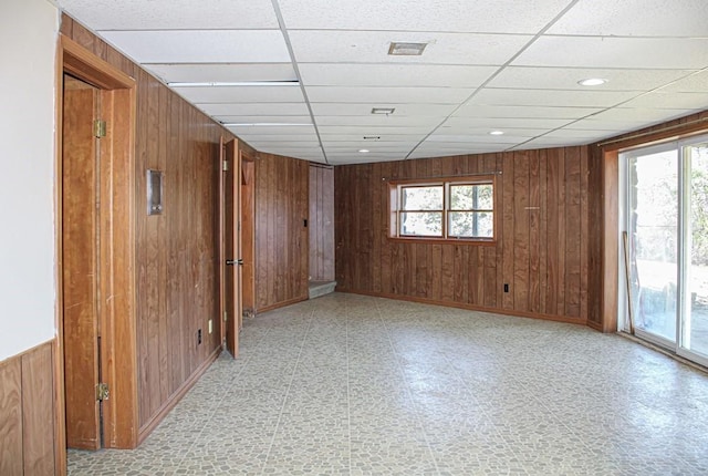 empty room featuring a paneled ceiling and wood walls