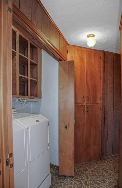 clothes washing area with wood walls, a textured ceiling, and independent washer and dryer