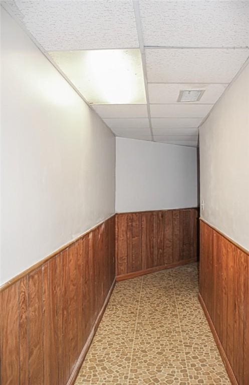 hallway with wood walls and a drop ceiling