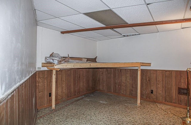 basement featuring wooden walls and a drop ceiling