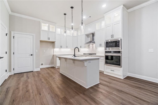 kitchen featuring oven, white cabinets, wall chimney exhaust hood, an island with sink, and built in microwave