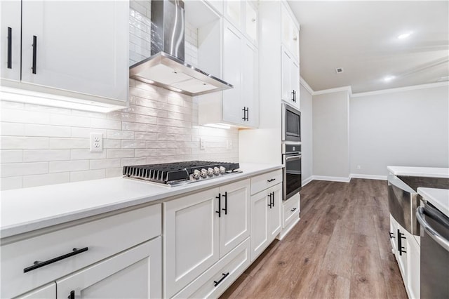 kitchen featuring light hardwood / wood-style floors, stainless steel appliances, white cabinetry, and wall chimney exhaust hood