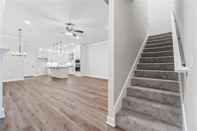 stairway with sink, hardwood / wood-style floors, ceiling fan with notable chandelier, and ornamental molding