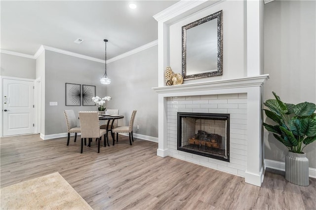 dining space featuring a brick fireplace, hardwood / wood-style floors, and crown molding