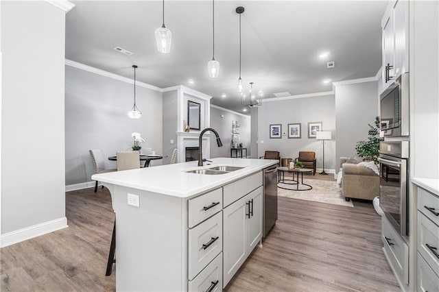 kitchen featuring a center island with sink, white cabinetry, hanging light fixtures, and sink