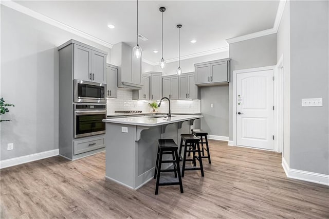 kitchen featuring sink, tasteful backsplash, gray cabinets, a center island with sink, and appliances with stainless steel finishes