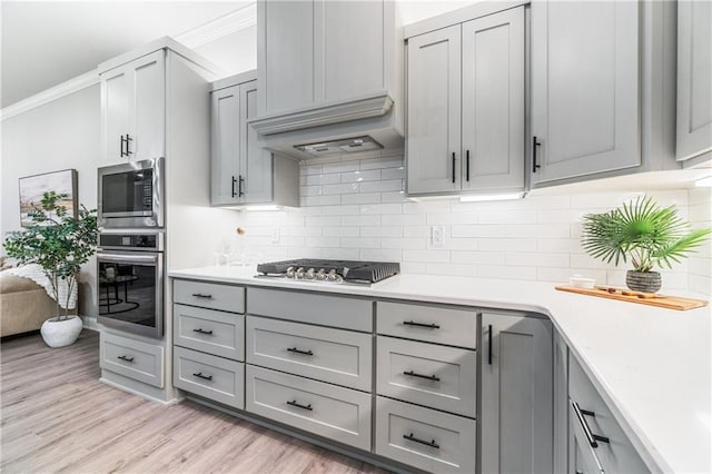 kitchen featuring gray cabinets, stainless steel appliances, light wood-type flooring, ornamental molding, and decorative backsplash