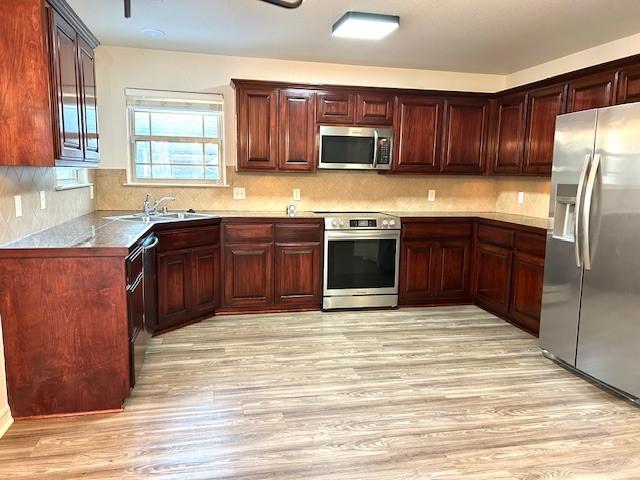 kitchen with stainless steel appliances, sink, light wood-type flooring, and tasteful backsplash