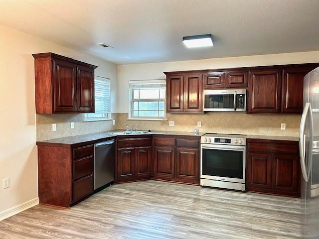 kitchen with appliances with stainless steel finishes, light hardwood / wood-style flooring, decorative backsplash, and sink