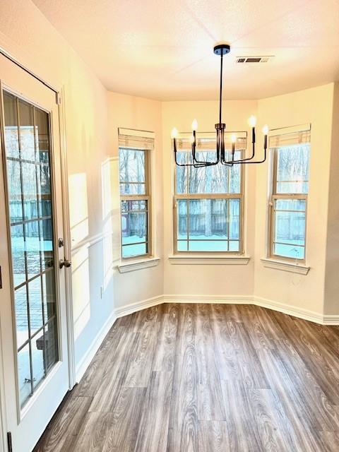 unfurnished dining area with dark wood-type flooring, an inviting chandelier, and a healthy amount of sunlight