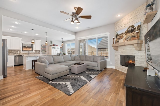 living room with a ceiling fan, baseboards, recessed lighting, a fireplace, and light wood-type flooring