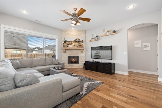 living area featuring light wood-type flooring, recessed lighting, arched walkways, a stone fireplace, and baseboards