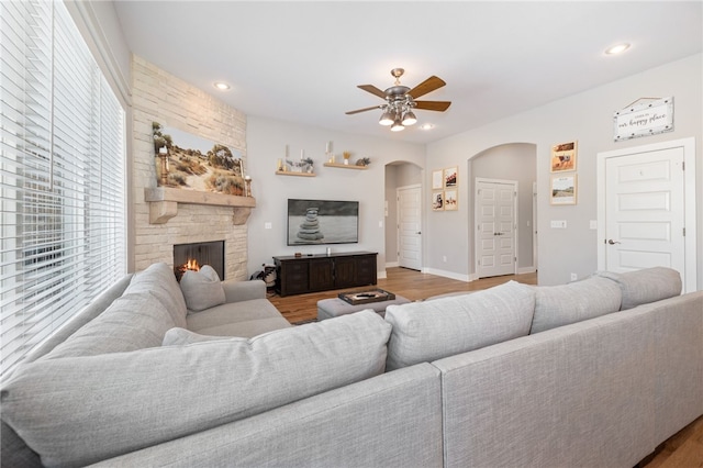 living area featuring wood finished floors, recessed lighting, a fireplace, arched walkways, and ceiling fan