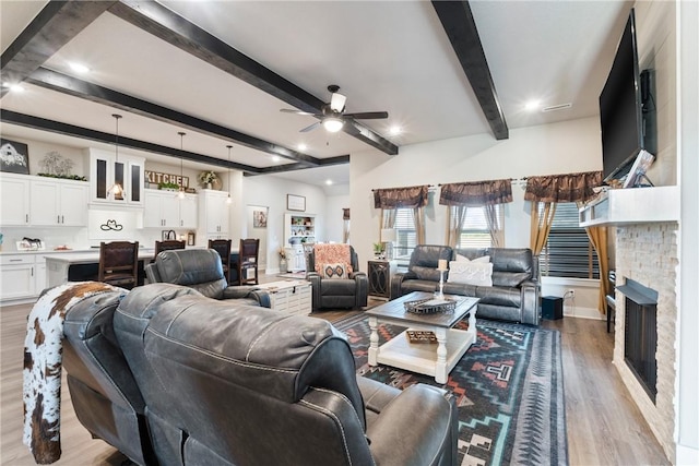 living room featuring light wood-type flooring, beam ceiling, ceiling fan, and a stone fireplace