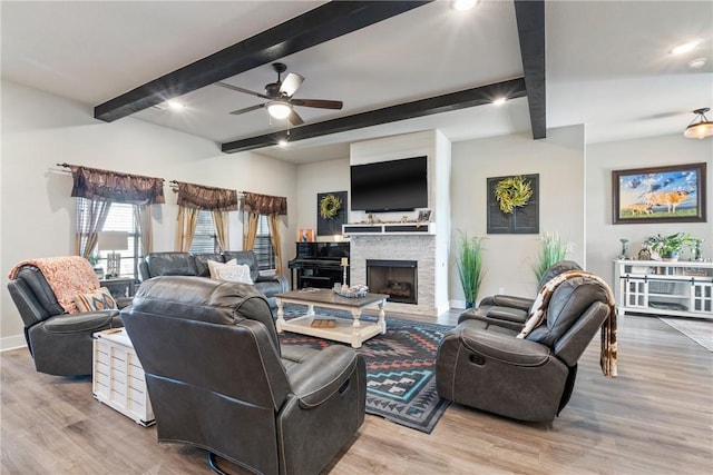 living room featuring light wood-type flooring, beam ceiling, ceiling fan, and a stone fireplace