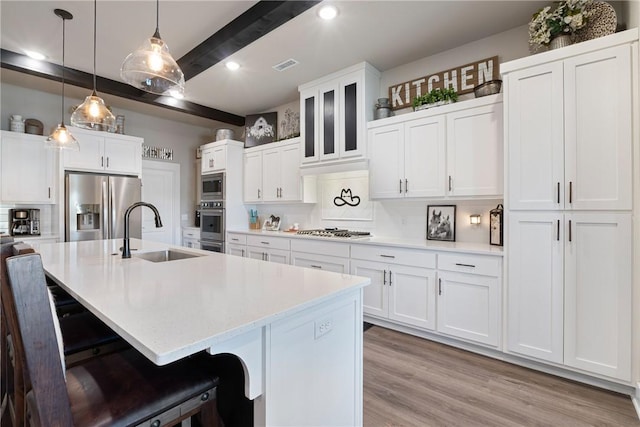 kitchen with appliances with stainless steel finishes, white cabinetry, a kitchen island with sink, and sink