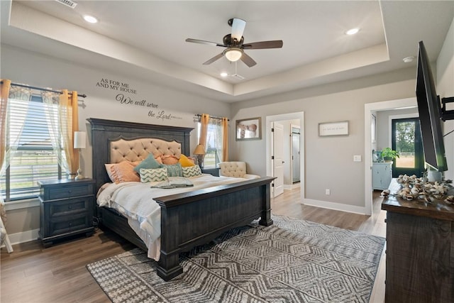 bedroom with hardwood / wood-style floors, ceiling fan, and a tray ceiling