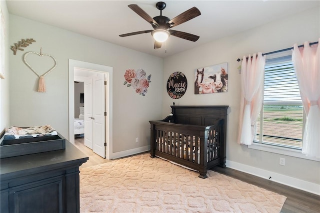 bedroom featuring a nursery area, connected bathroom, ceiling fan, and light wood-type flooring